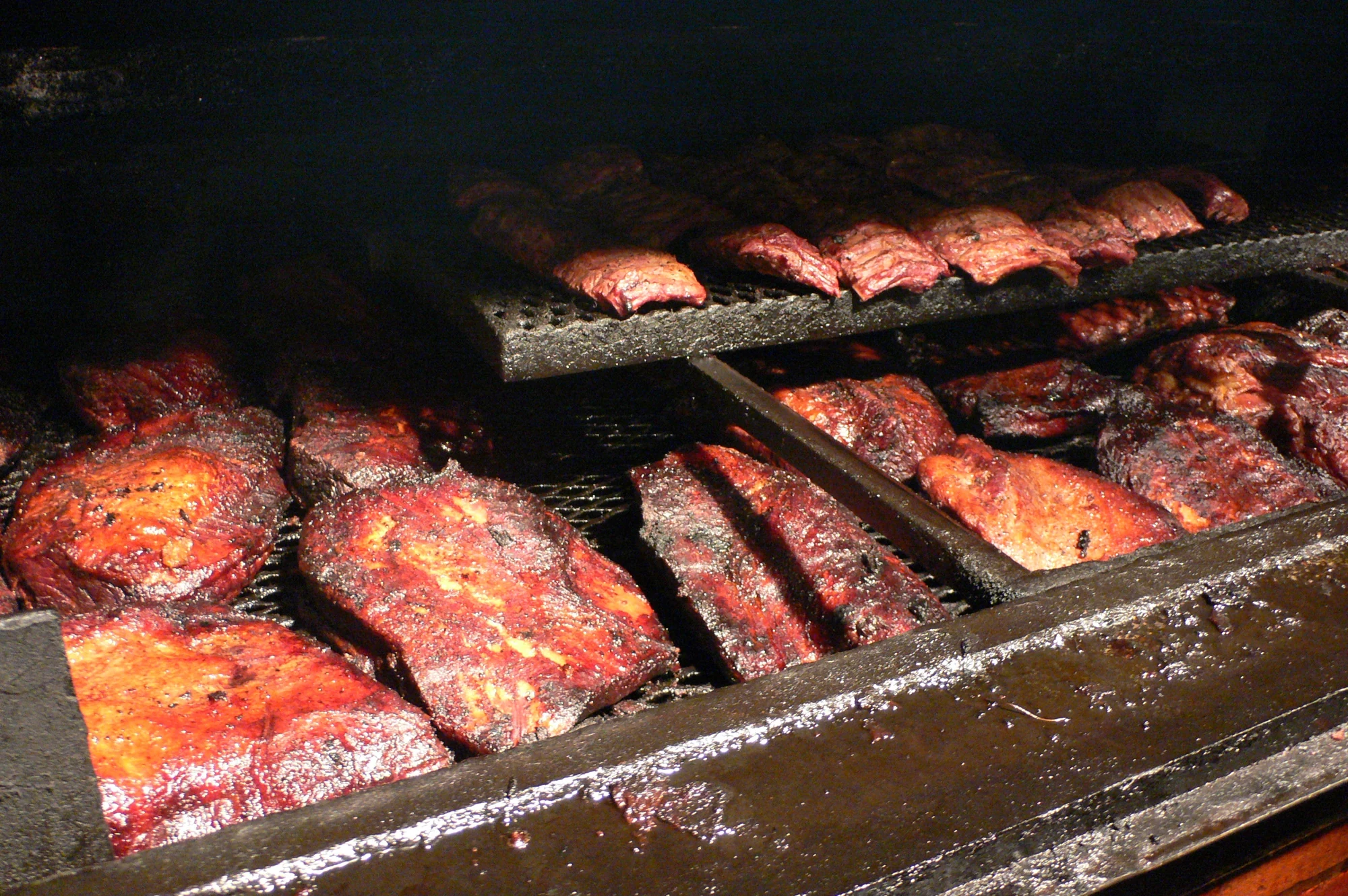 Briskets and ribs cooking on racks inside a barbecue smoker
