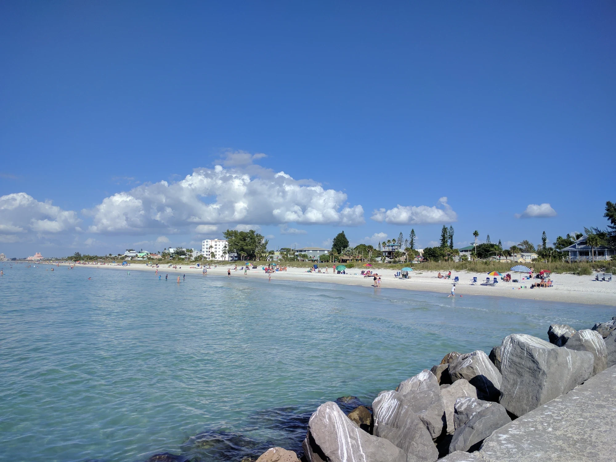 Pass-a-Grille Beach seen from a rocky pier, with swimmers and beach umbrellas