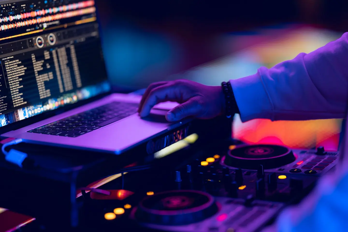 A DJ using a laptop and controller under blue and purple lighting